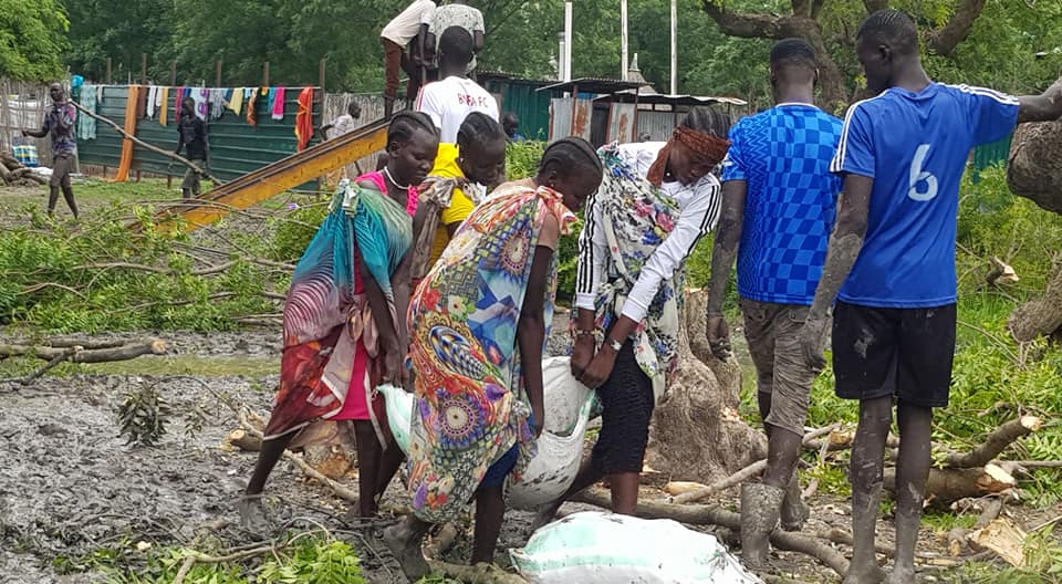 Students carry heavy bags of sand across a muddy path to help build a bridge