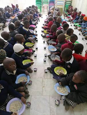 Kenyan preschoolers sit in a row eating bowls of porridge