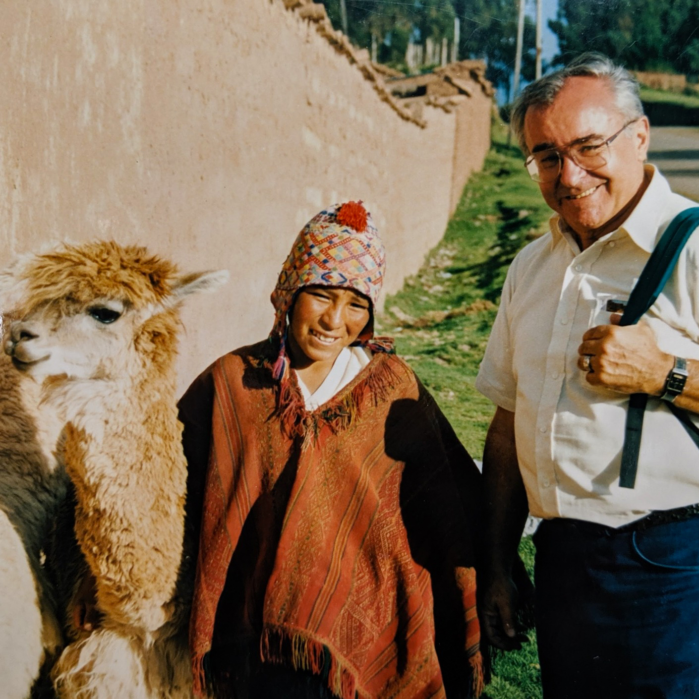 Fr Louie stands next to a young peruvian farmer and their llama