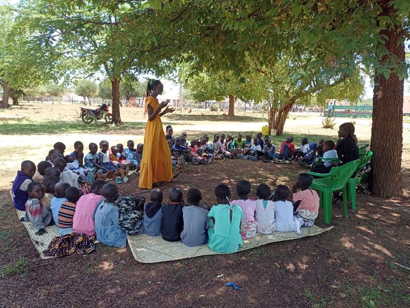 Students sit under a mango tree in an outdoor Kenyan classroom<br />

