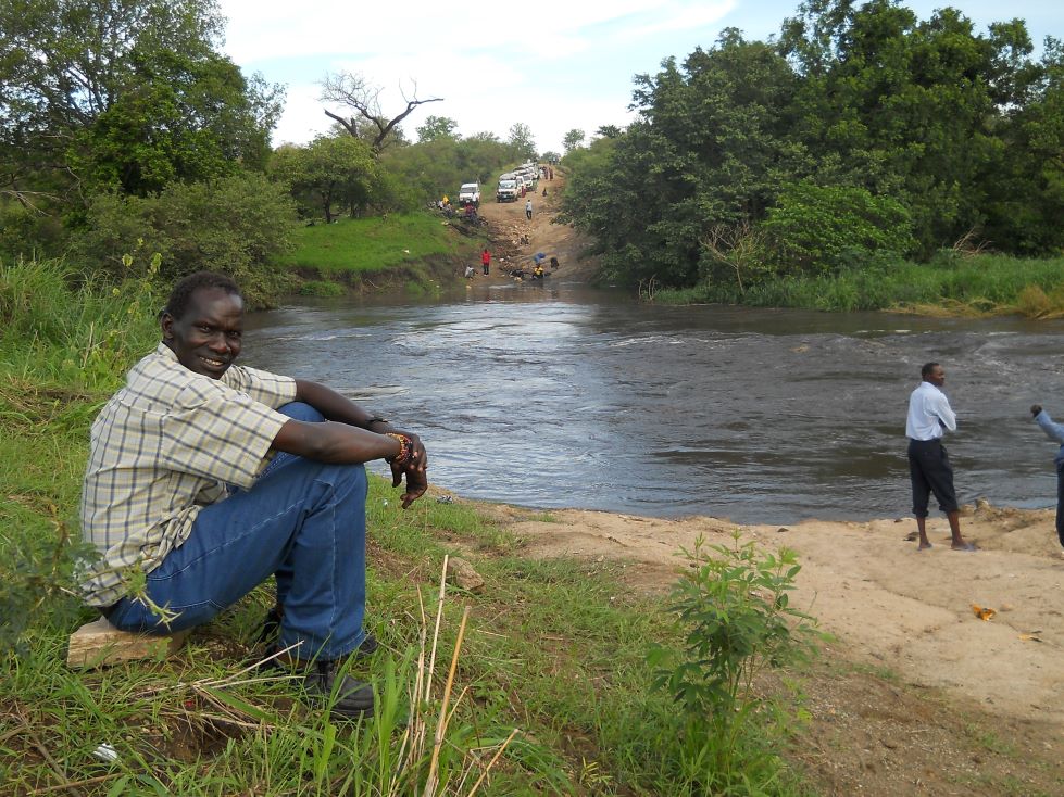 Fr Louis Ochermoi sits on the bank of a river in Africa.