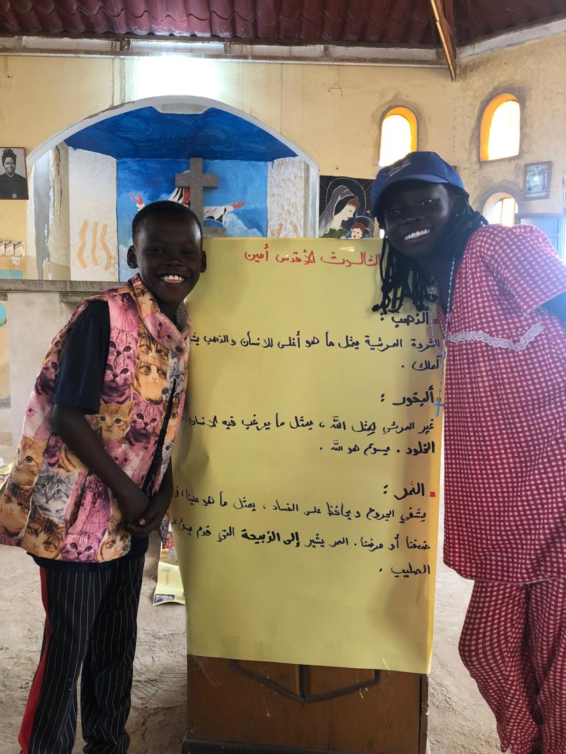 Two young african girls pose next a sign in Arabic