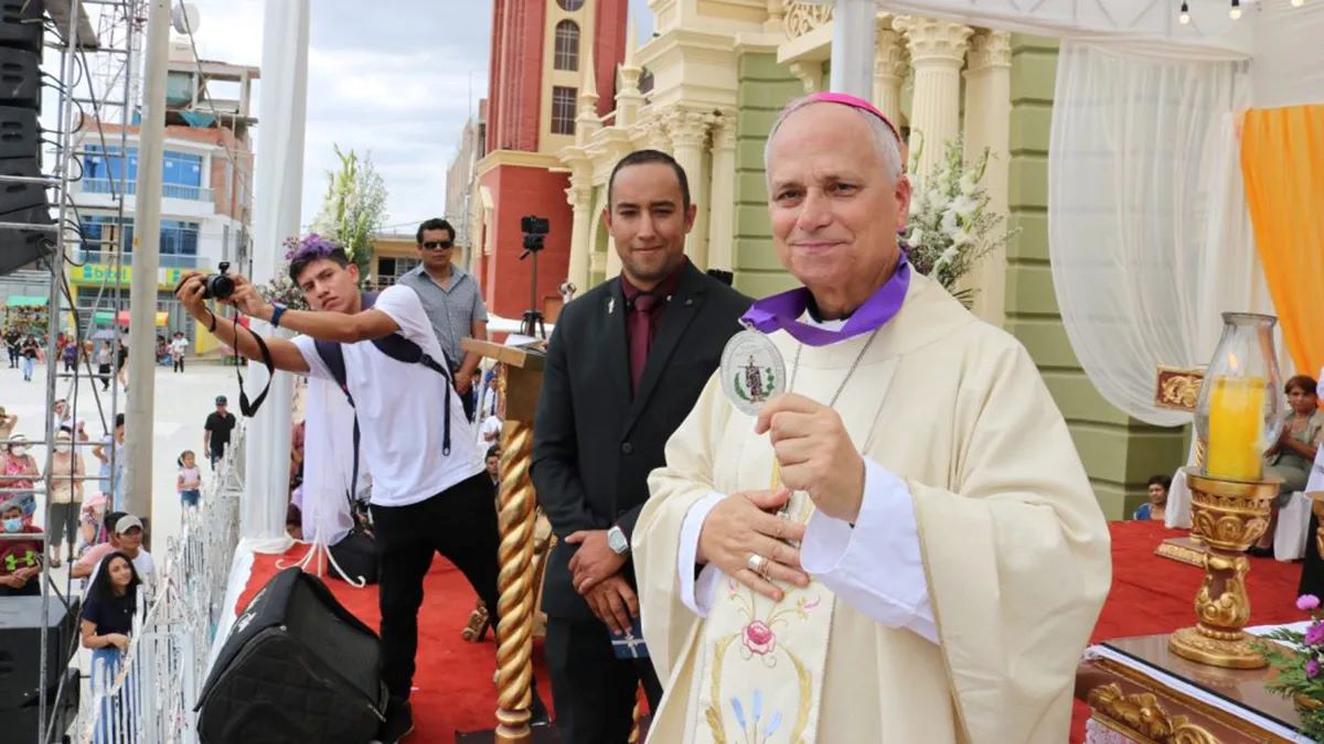 Pope Leo, dressed in his Cardinal robes, holds out a medal, at a celebration in Peru